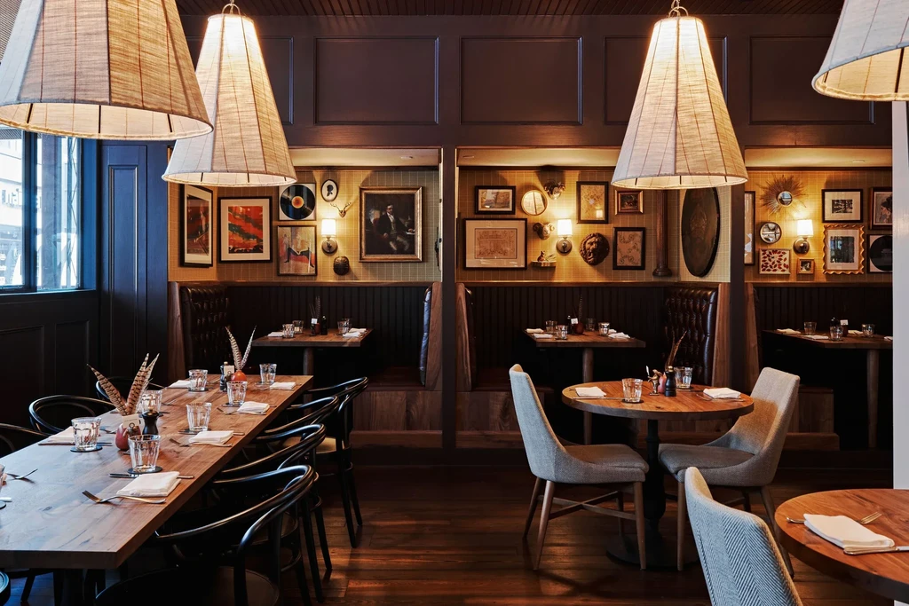 Restaurant interior with a long communal table, booths, and eclectic wall decor.