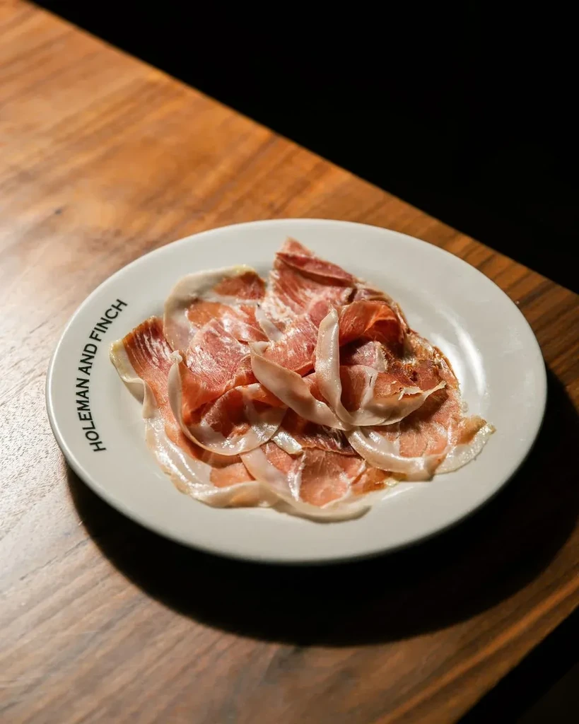 Marbled cured meat slices on a 'HOLEMAN AND FINCH' branded plate.