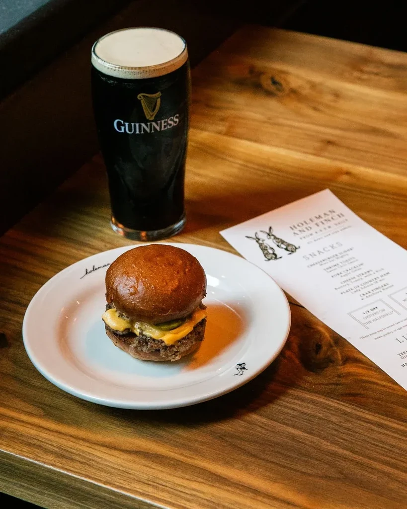 A slider, Guinness beer, and menu on a rustic wooden table.
