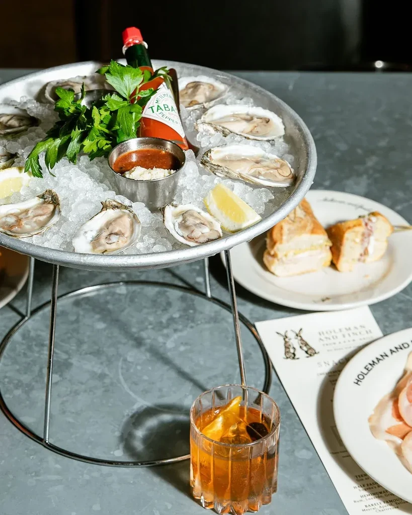 Top-down view: Dozen oysters on ice, sauces, and drinks on a table.