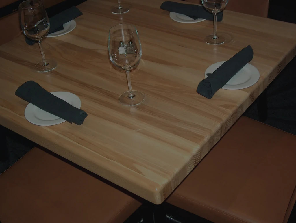 Light wooden dining table set for four with plates, napkins, glasses.