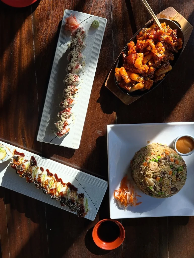 Overhead view of sushi, stir-fry, and fried rice on a wooden table.