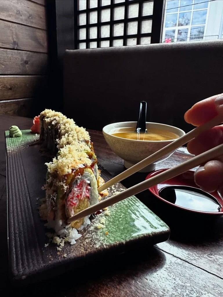 Hand with chopsticks reaching for a tempura-topped sushi roll.