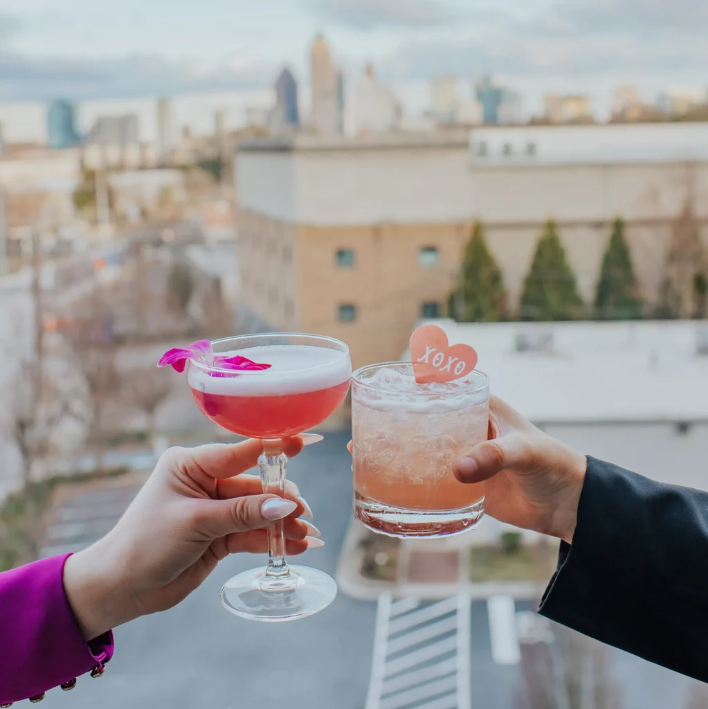 Hands holding orchid and xoxo cocktails, city skyline.