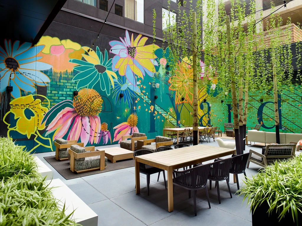 Outdoor patio with colorful floral mural, modern furniture, trees, and plants.