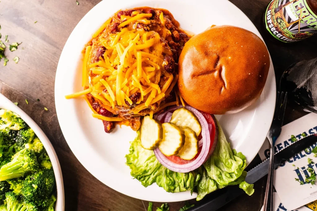 Close-up chili cheese burger, bun, broccoli, and craft beverage.
