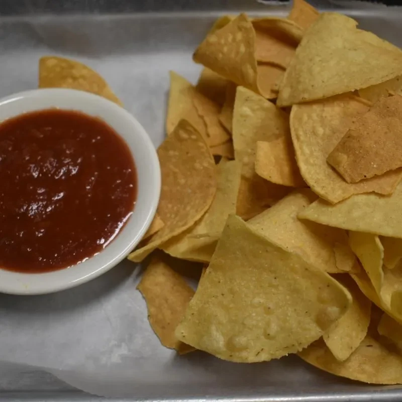 Chunky red salsa in a white bowl with a pile of tortilla chips.