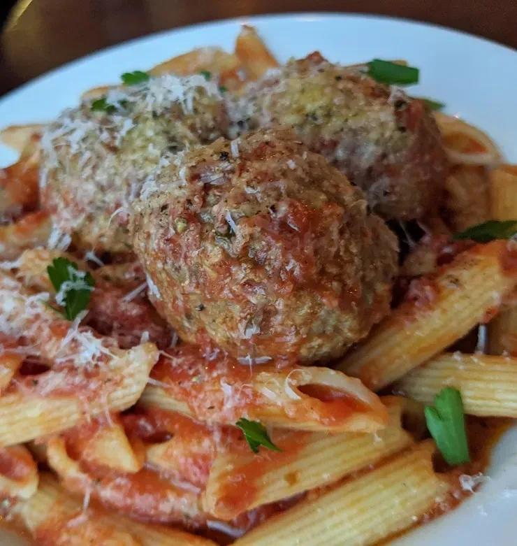 Penne pasta with three meatballs, tomato sauce, grated cheese, and herbs.