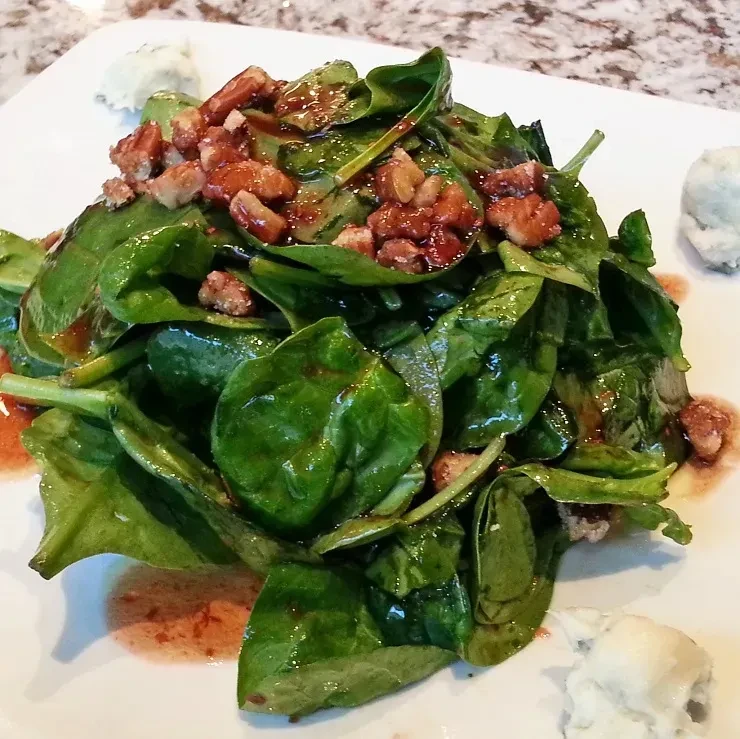 Fresh spinach salad with vinaigrette, candied pecans, and white garnish.
