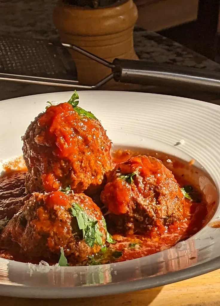 Three meatballs with tomato sauce, fresh herbs, and grated cheese.