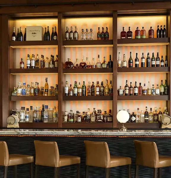 Well-stocked bar wall with backlit liquor bottles and leather bar stools.