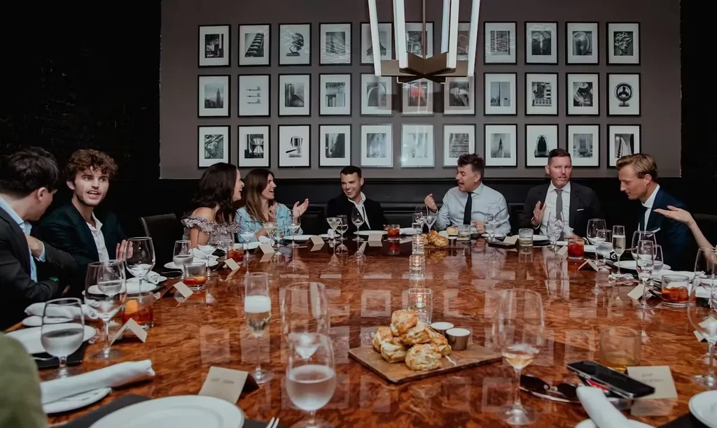 Guests enjoying food and drinks around an elegantly set dark wood table.