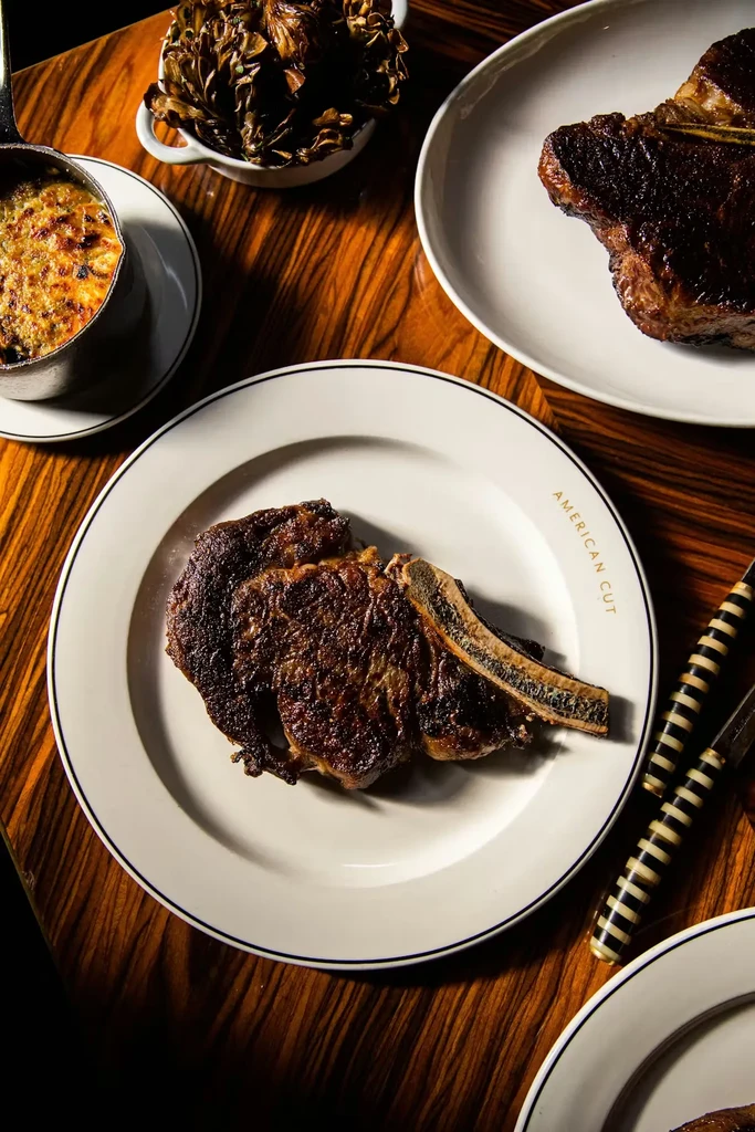 Overhead: Bone-in steak, bubbling gratin, and sides on dark wood.