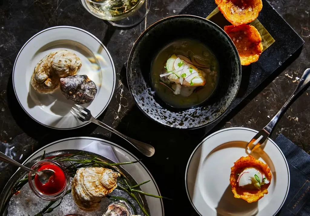 Top-down view of raw oysters, ceviche, and crispy cups on marble.