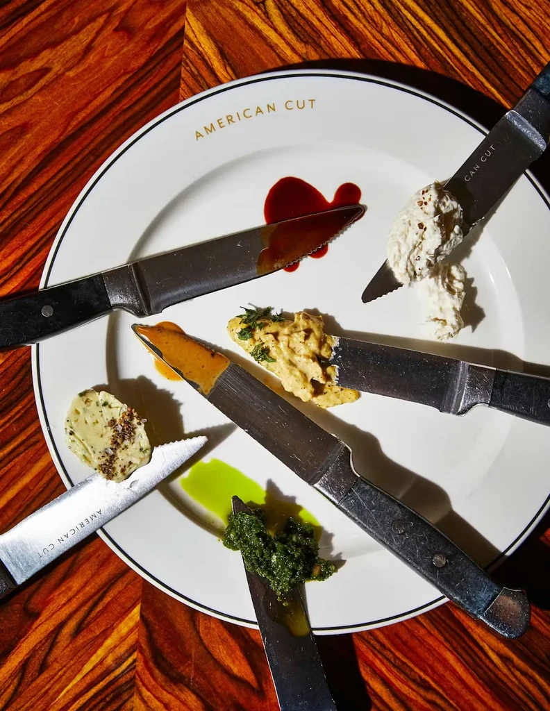 Overhead: American Cut plate, six steak knives radially holding sauces.