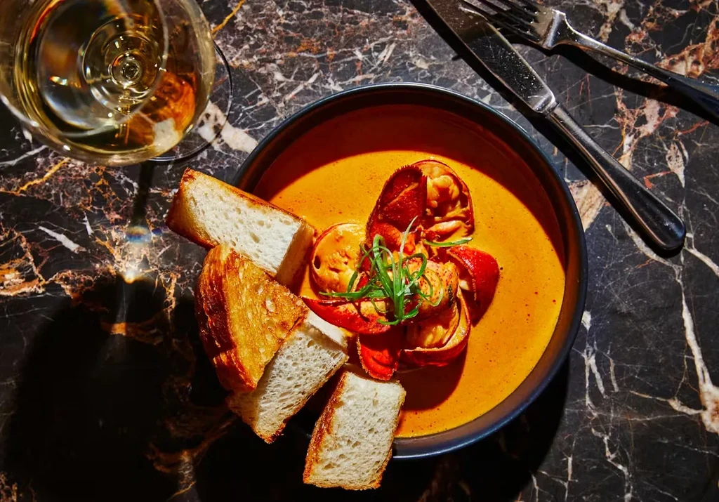 Overhead view of lobster bisque, bread, wine, and cutlery on marble.