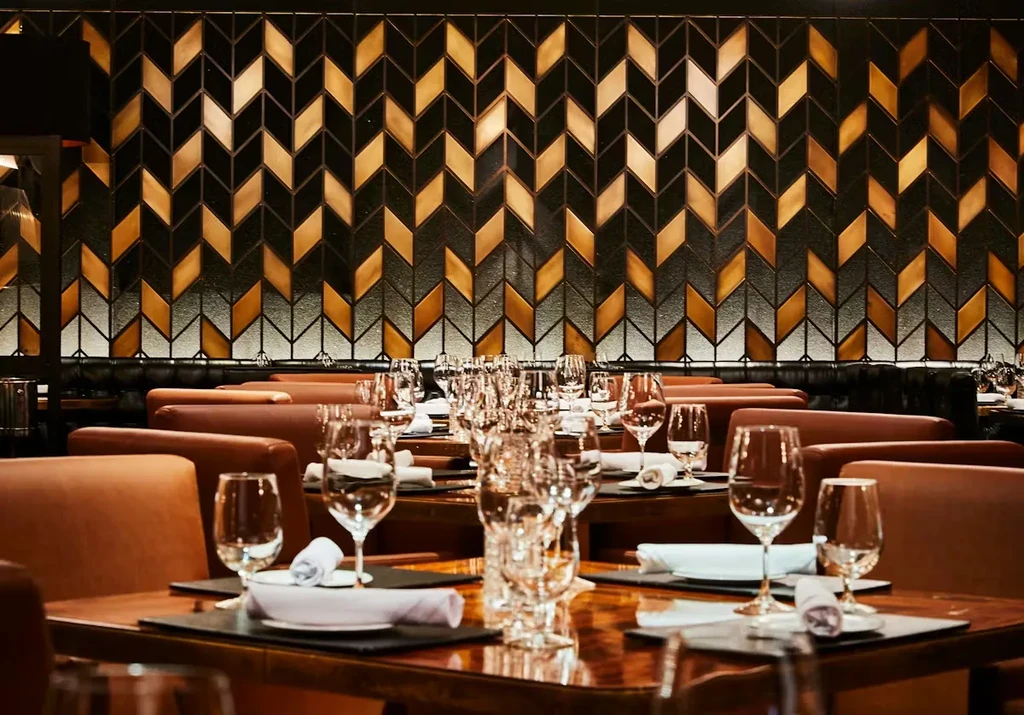 Modern restaurant interior with set tables and a gold geometric wall.