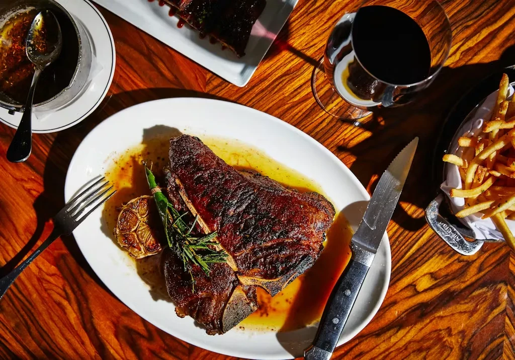 Overhead T-bone steak meal with ribs, fries, and red wine.