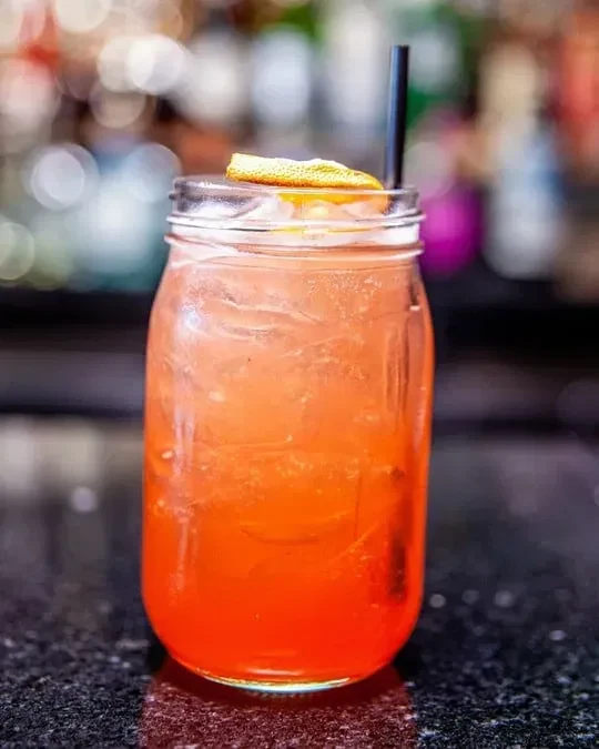 Red-orange carbonated drink in a mason jar with ice, citrus.