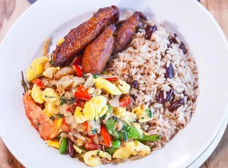 Close-up of Caribbean meal: ackee, saltfish, rice, peas, fried plantain.