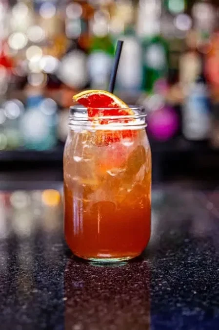 Reddish-orange cocktail in a mason jar with citrus garnish.