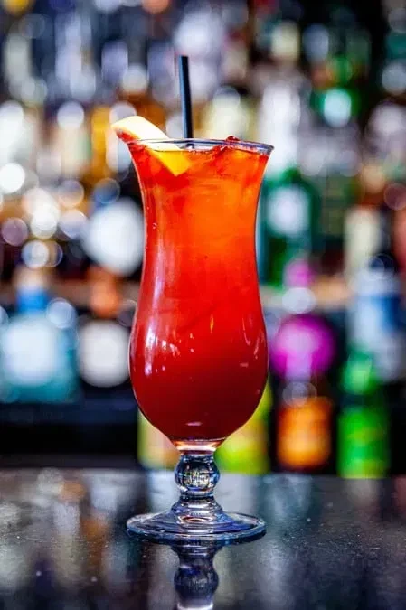 Layered red and orange cocktail in a hurricane glass with citrus.