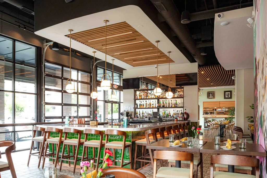 Empty modern restaurant interior featuring green-tiled bar and dining tables.