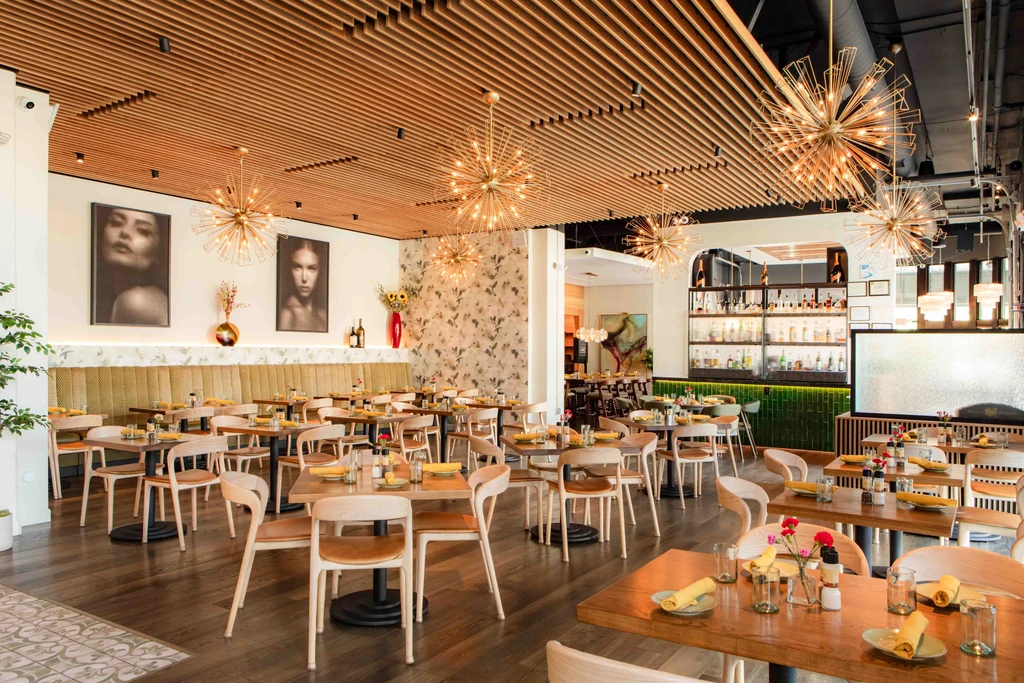 Unoccupied contemporary restaurant interior with dining area, bar, and sputnik chandeliers.