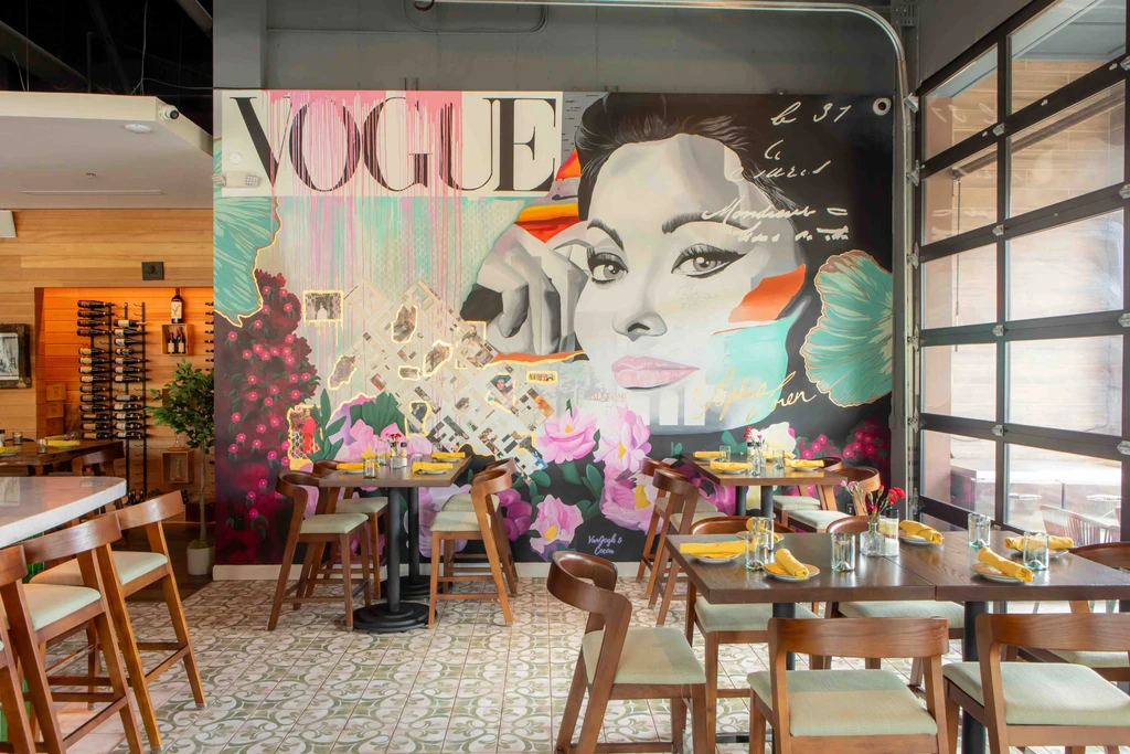 Vibrant restaurant interior with large 'VOGUE' mural, dining tables, and bar.