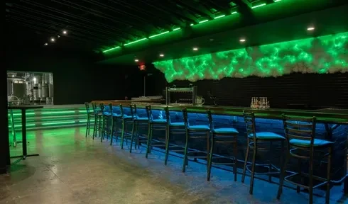 Modern brewery taproom with blue-lit bar, green neon, brewing equipment.