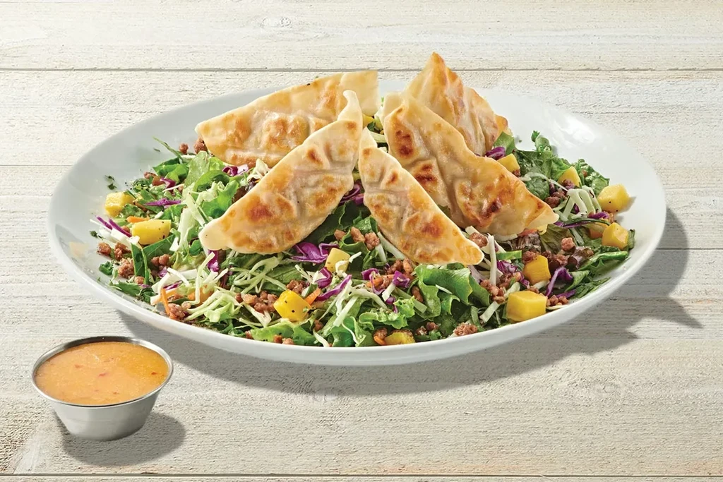 Salad with pan-fried dumplings, greens, meat, diced fruit, and orange dressing.