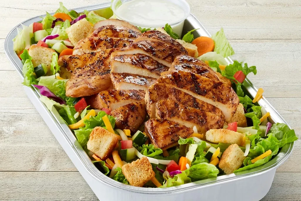 Grilled chicken salad with fresh vegetables and dressing in a container.