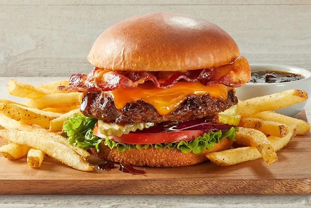 Detailed bacon cheeseburger with fries on a rustic cutting board.