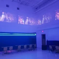 Modern event room with blue/purple lighting, concert projections, and tables.