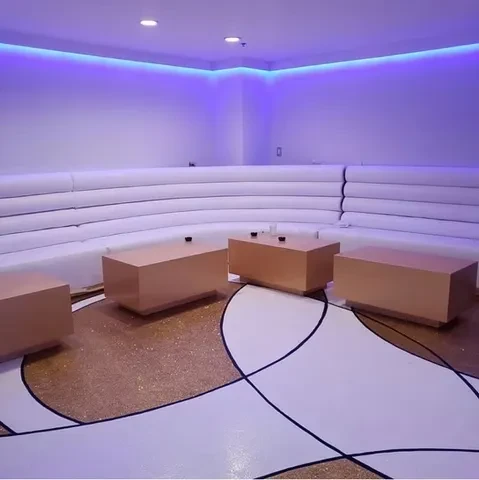 Modern lounge with curved white bench, metallic tables, purple lighting.