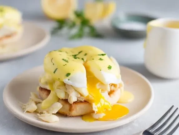 Eggs Benedict with runny yolk, hollandaise, and green garnish.