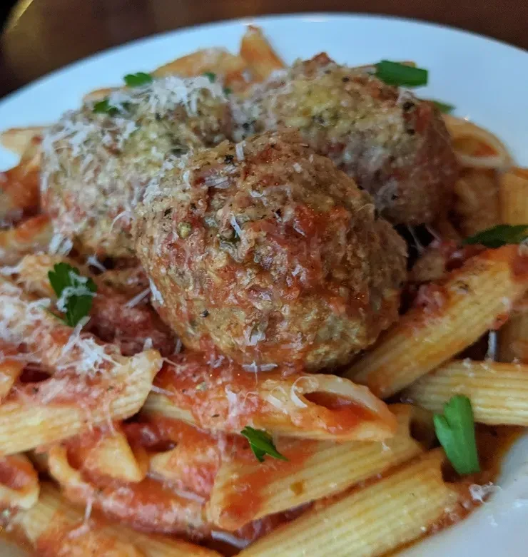 Close-up penne pasta with meatballs, tomato sauce, grated cheese, and herbs.