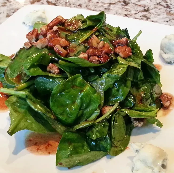 Spinach salad with candied nuts, glistening dressing, and white cheese.