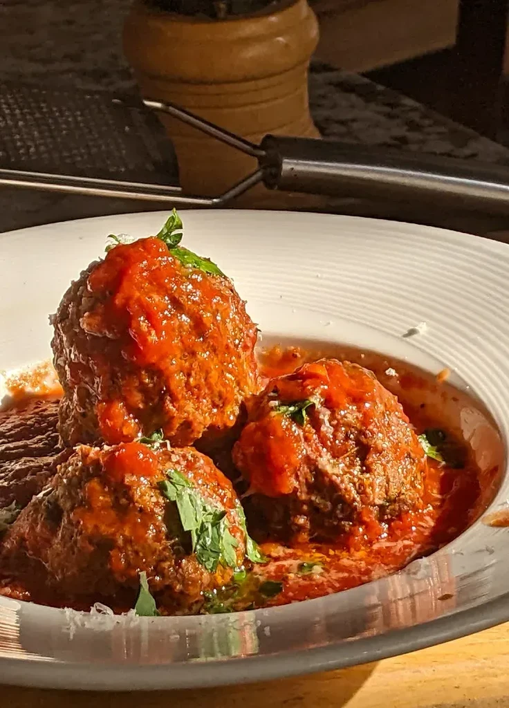Close-up of three meatballs with marinara, herbs, and cheese.