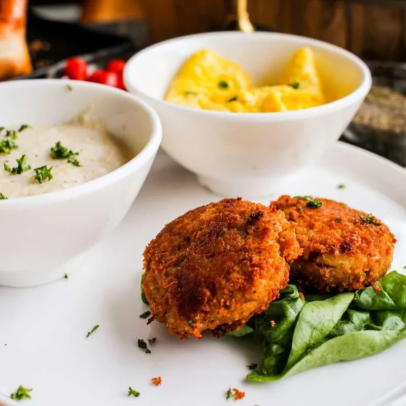 Two fried patties on greens, with creamy sauce and yellow side dish.