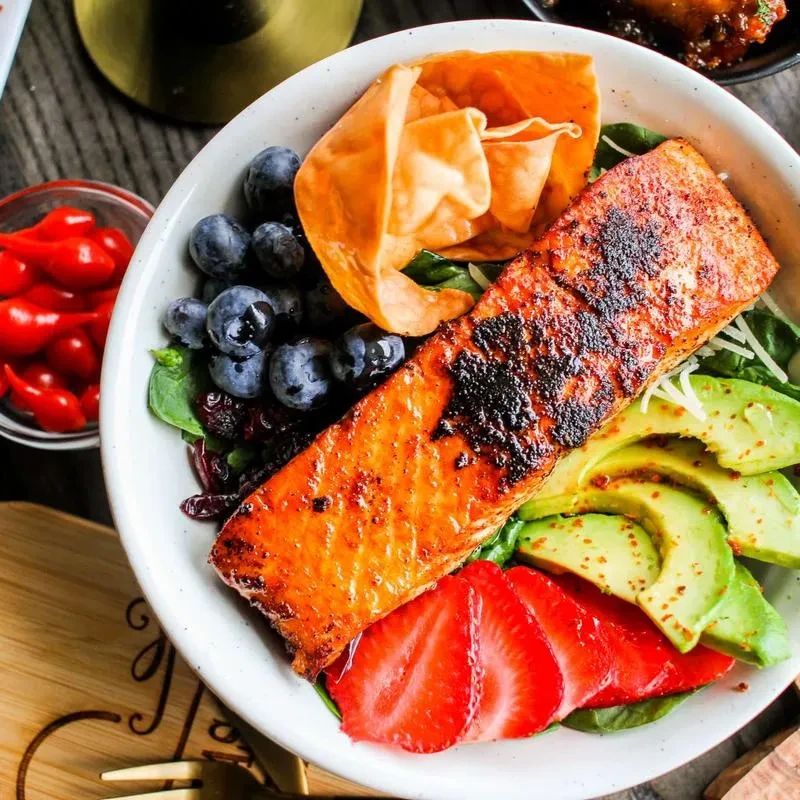 Overhead grilled salmon bowl with blueberries, avocado, strawberries, and greens.