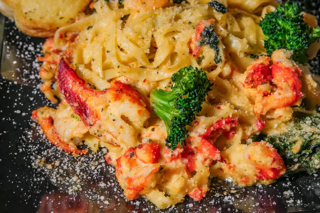Close-up of creamy lobster pasta with broccoli, Parmesan, and garlic bread.