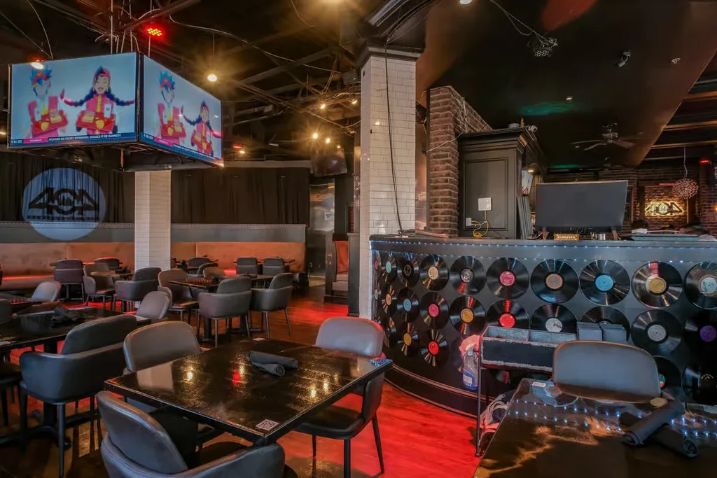 Dark, modern bar with red floor lights, pop culture screens, and vinyl decor.