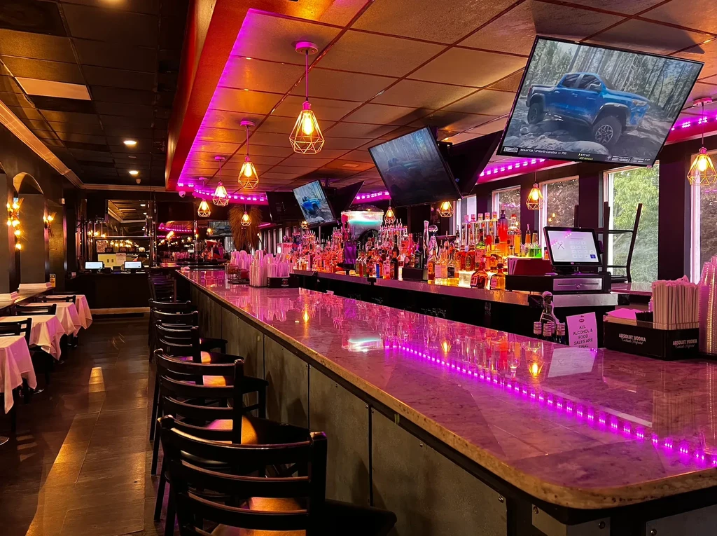 Pink LED-lit modern bar counter with tiered bottles and TVs.