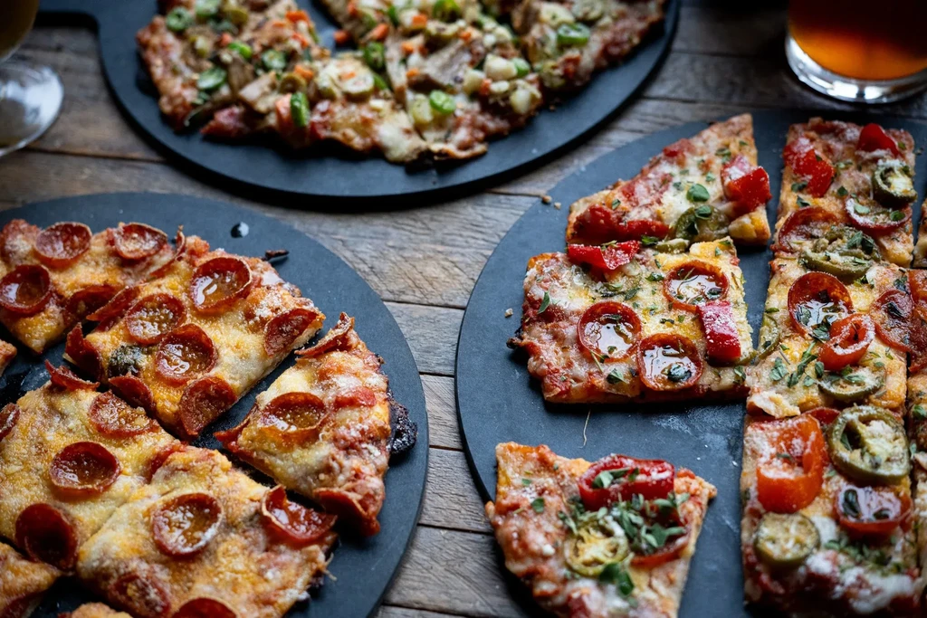 Three pizzas with pepperoni, mixed toppings, and vegetables on rustic table.