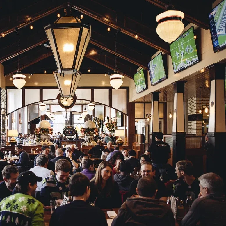 Bustling pub interior with patrons watching sports on wall-mounted TVs.