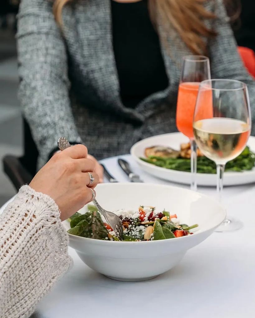Hand forks a salad with greens, cheese, and fruit at a restaurant.