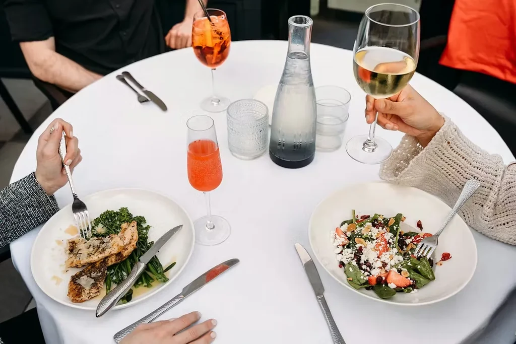 Overhead view of hands dining on chicken, salad, and drinks.