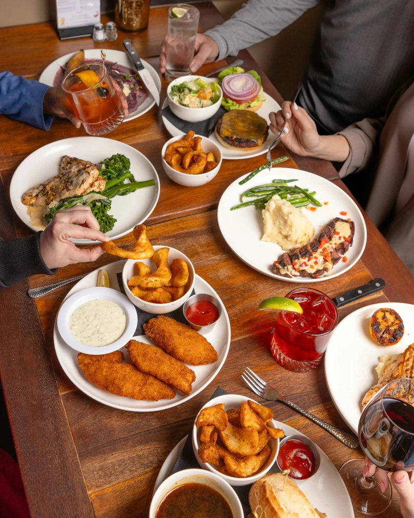Top-down view of a table with diverse food, drinks, and diners' hands.