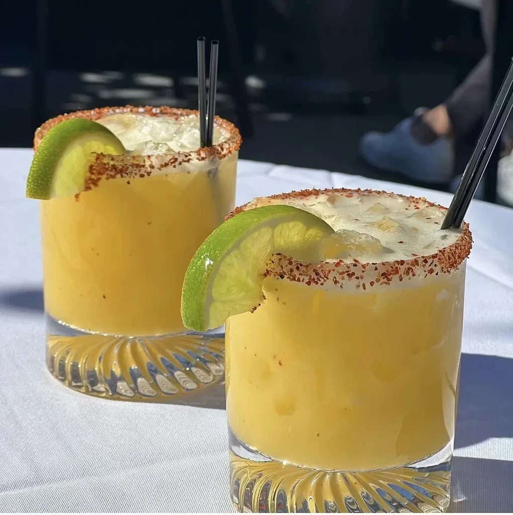 Two yellow-orange cocktails with spiced rims and lime wedges.